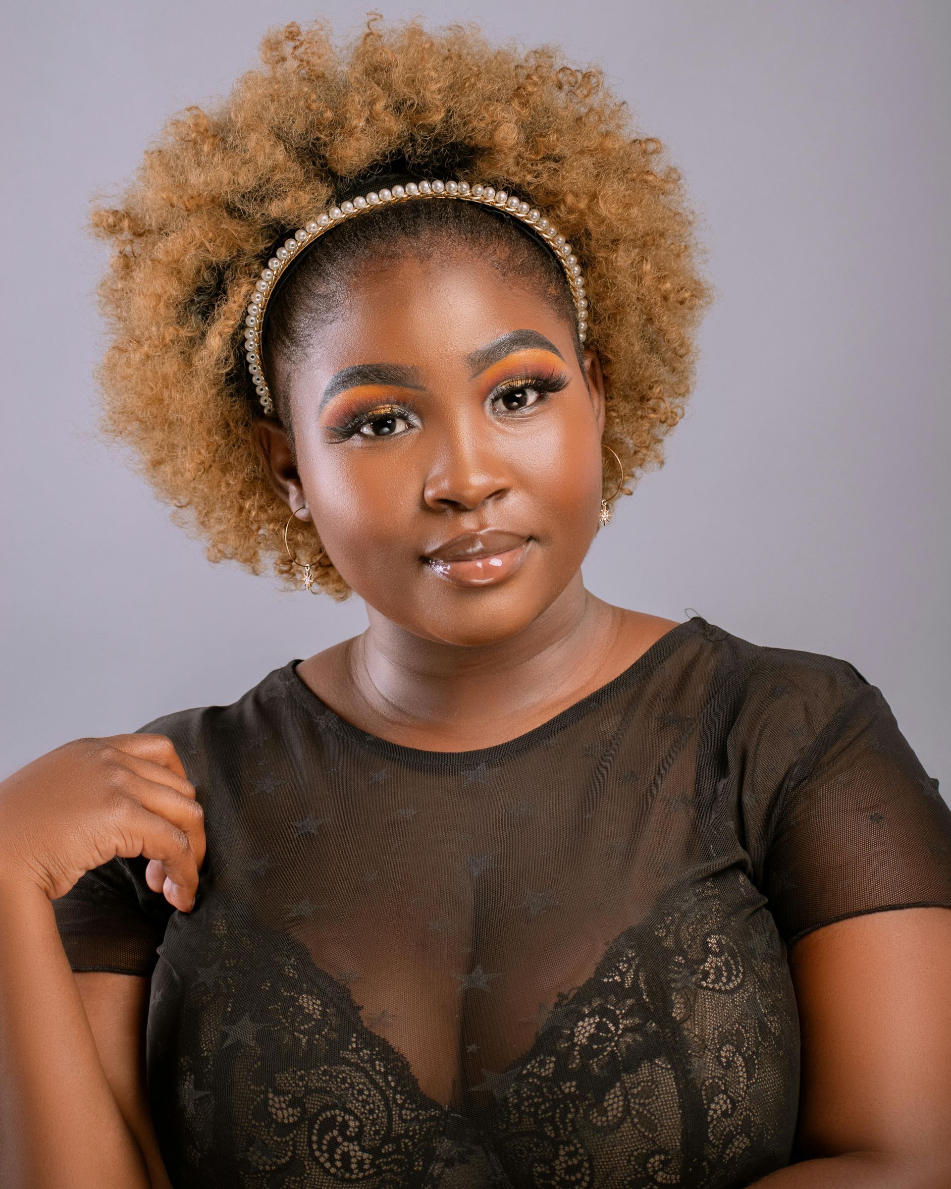 A woman with curly hair is wearing a headband and a black top.