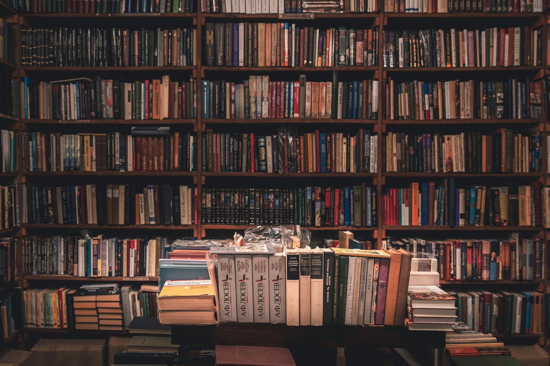 A library filled with lots of books and a stack of books on a table.
