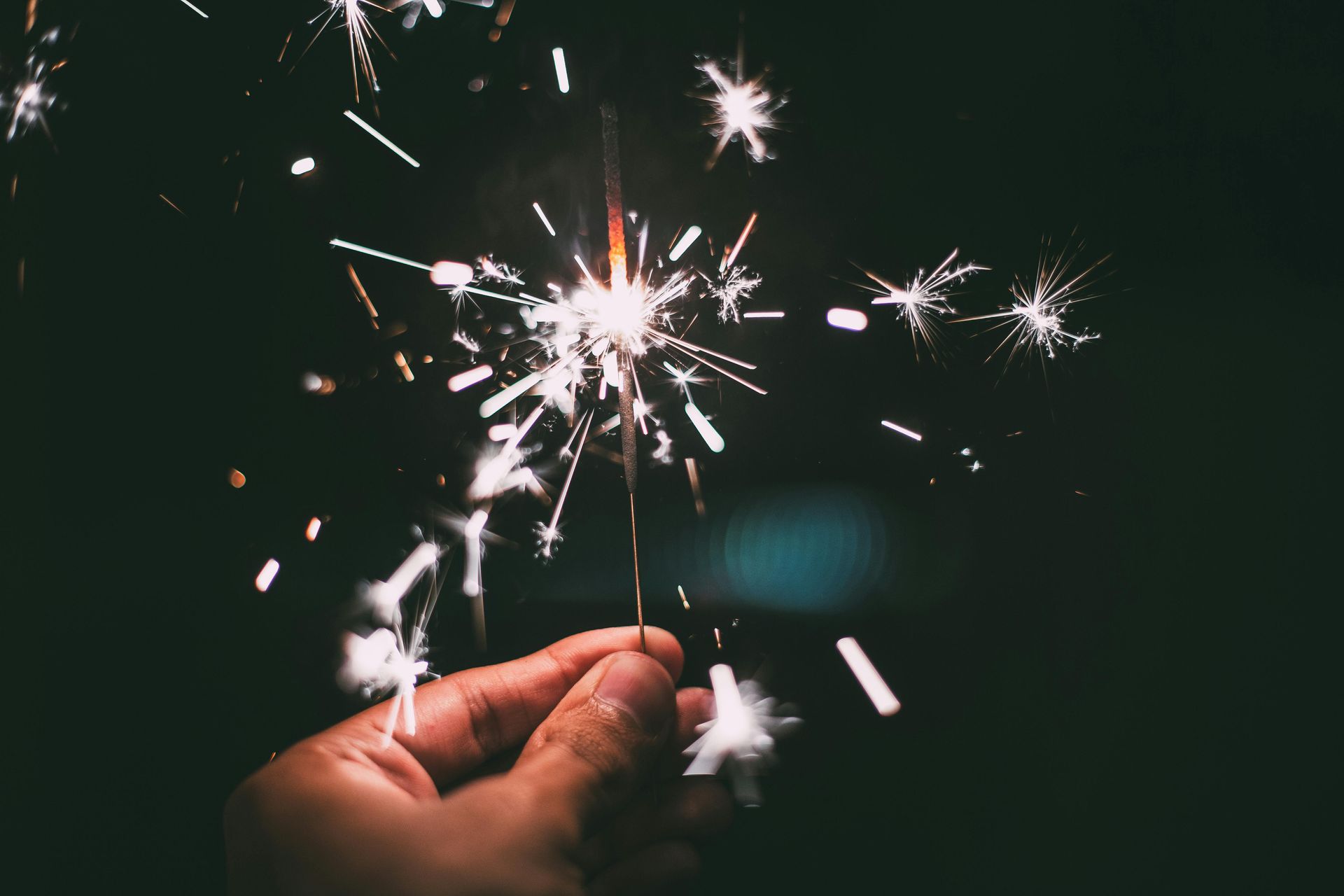 A person is holding a sparkler in their hand in the dark.