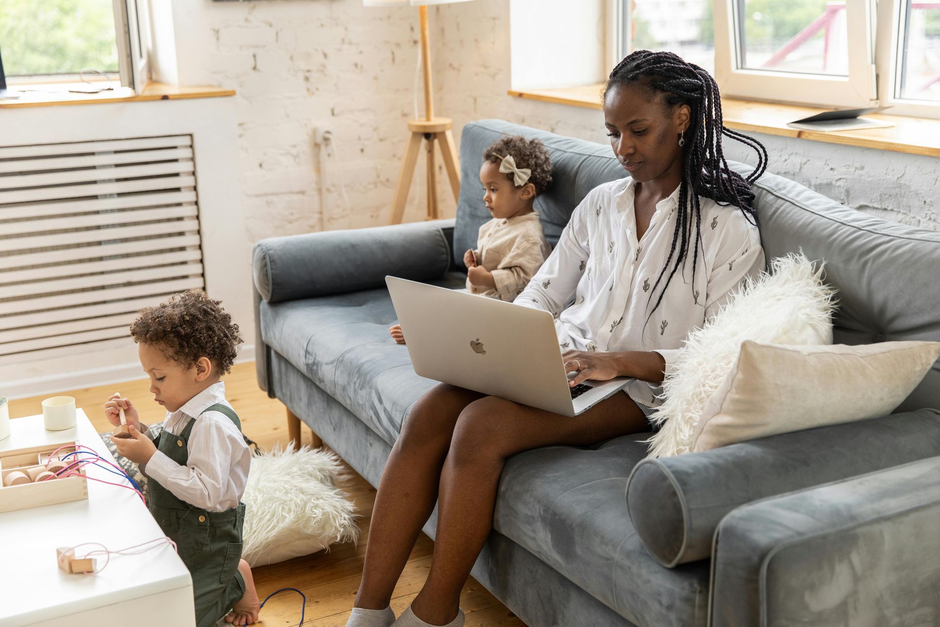 A woman is sitting on a couch with a laptop and two children.