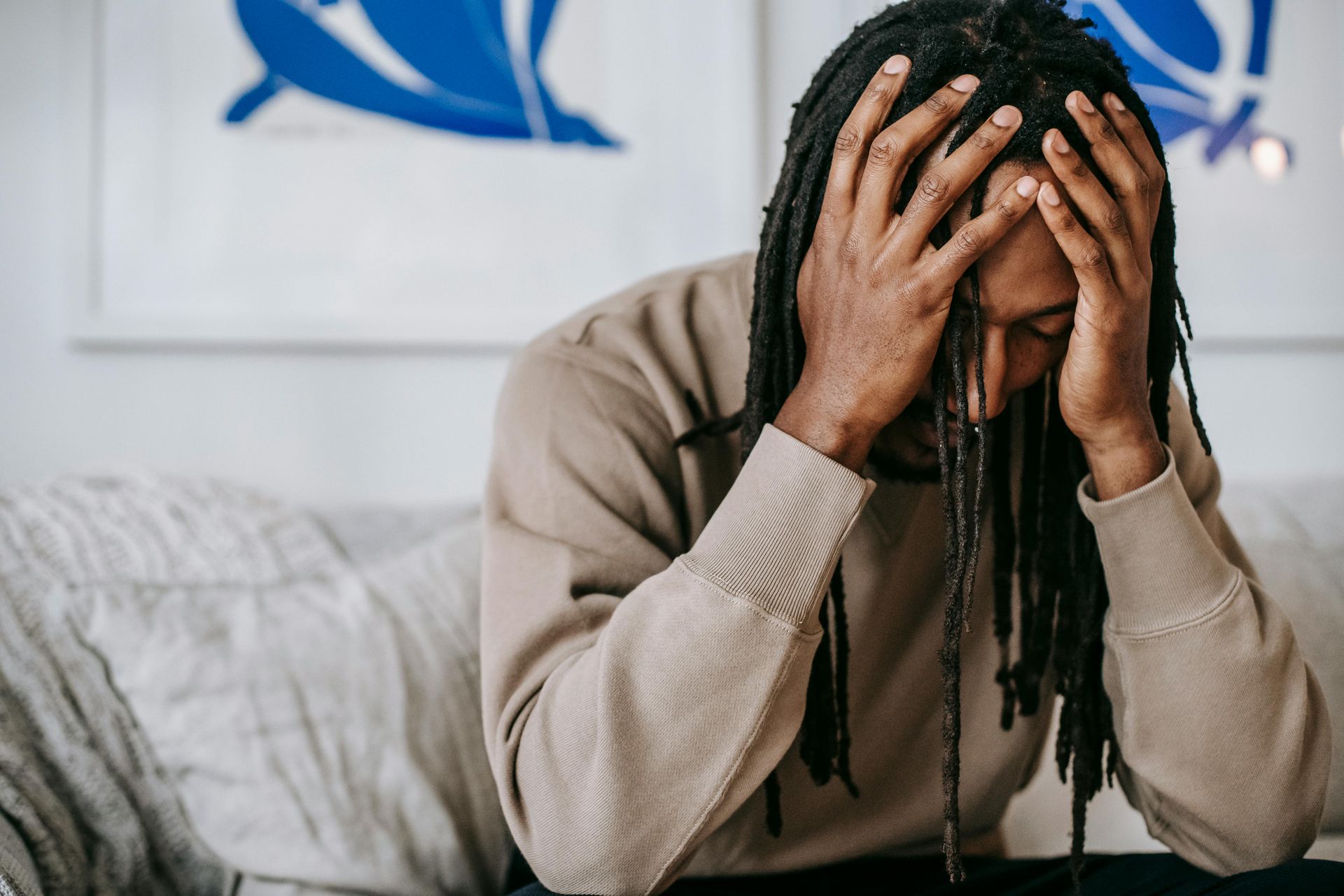 A man with dreadlocks is sitting on a couch with his hands on his head.