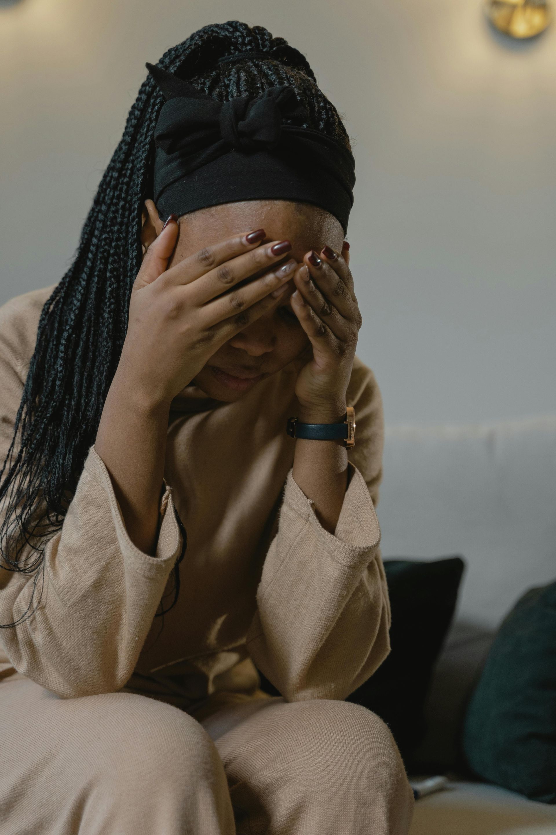 A woman is sitting on a couch covering her face with her hands.