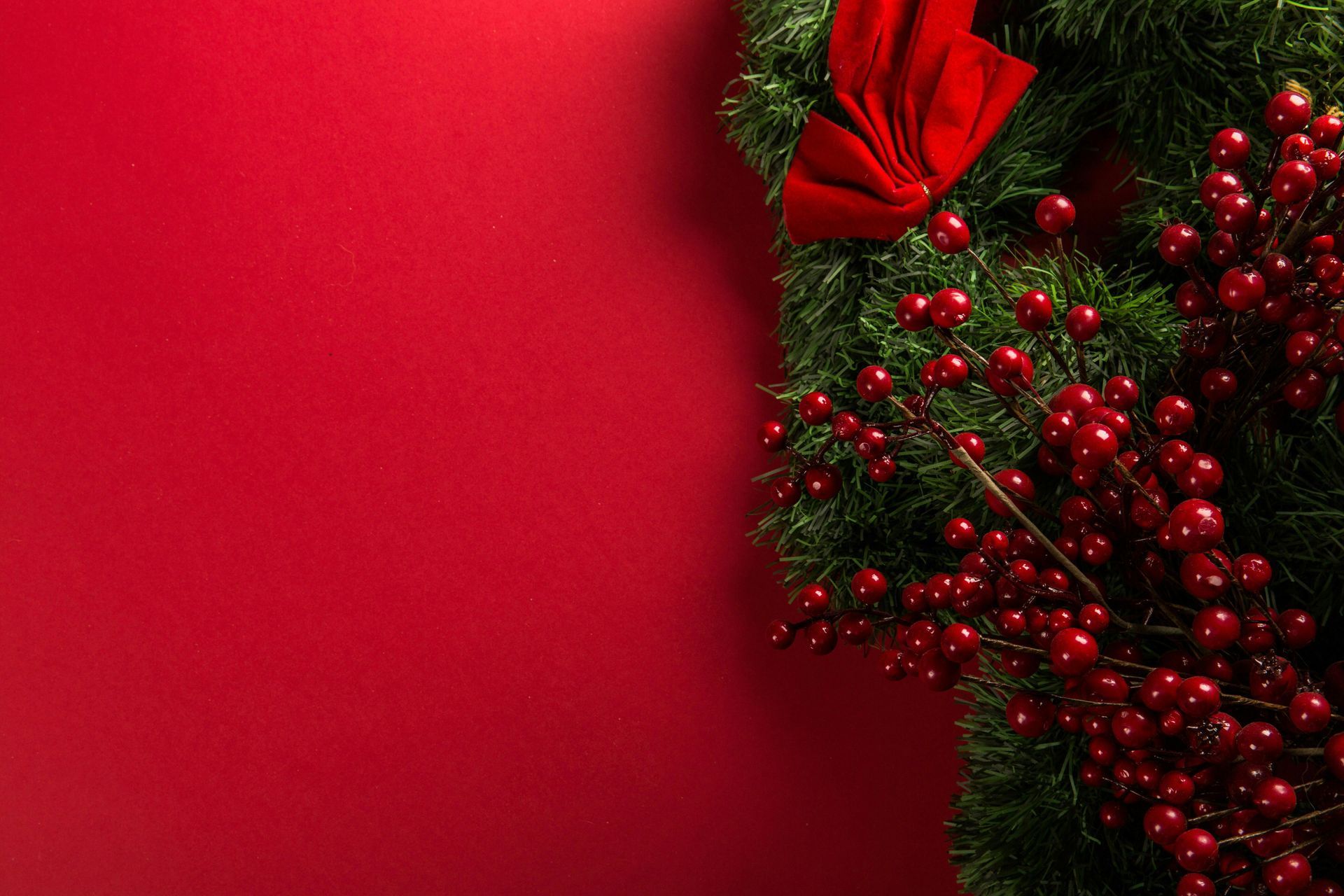 A christmas wreath with red berries and a red bow on a red background.