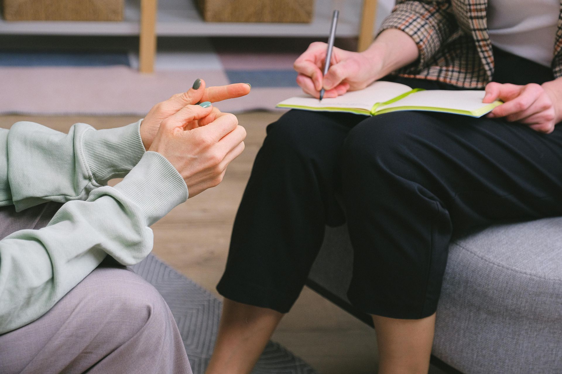 A woman is sitting on a couch talking to a man who is writing in a notebook.