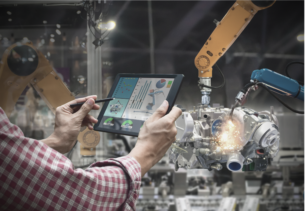 A man is using a tablet to control a robotic arm in a factory.