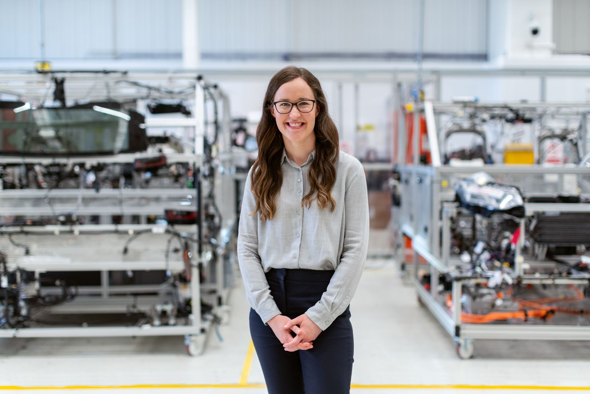 A woman is standing in front of a car in a factory.