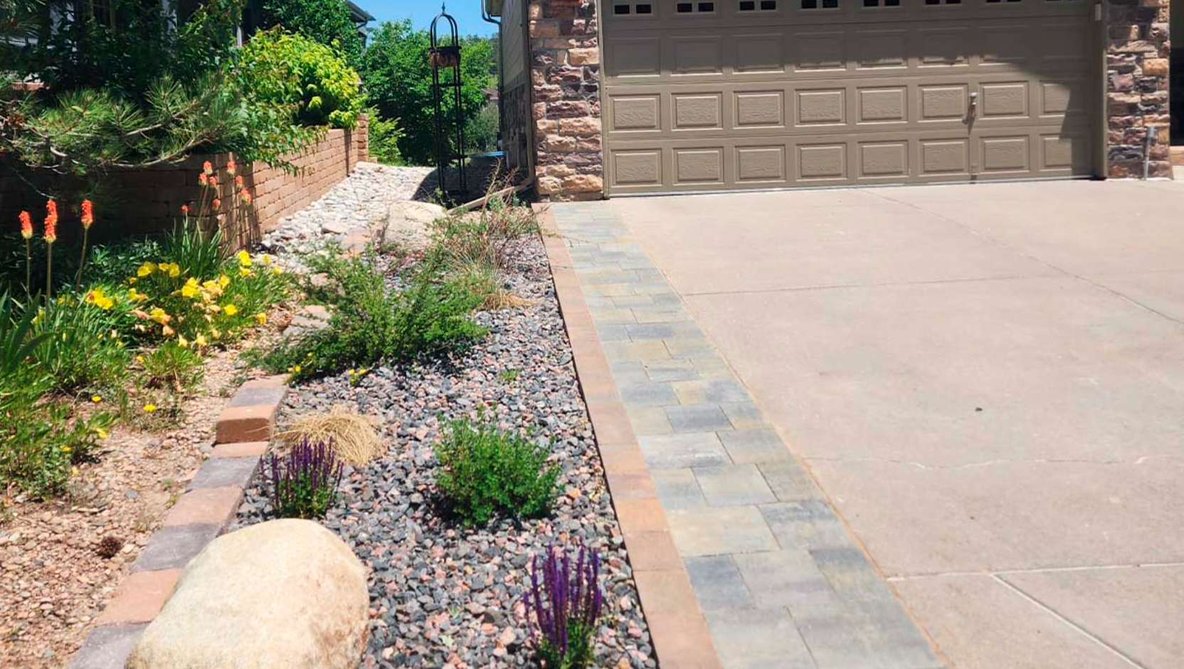 A driveway leading to a garage with flowers and rocks in front of it.