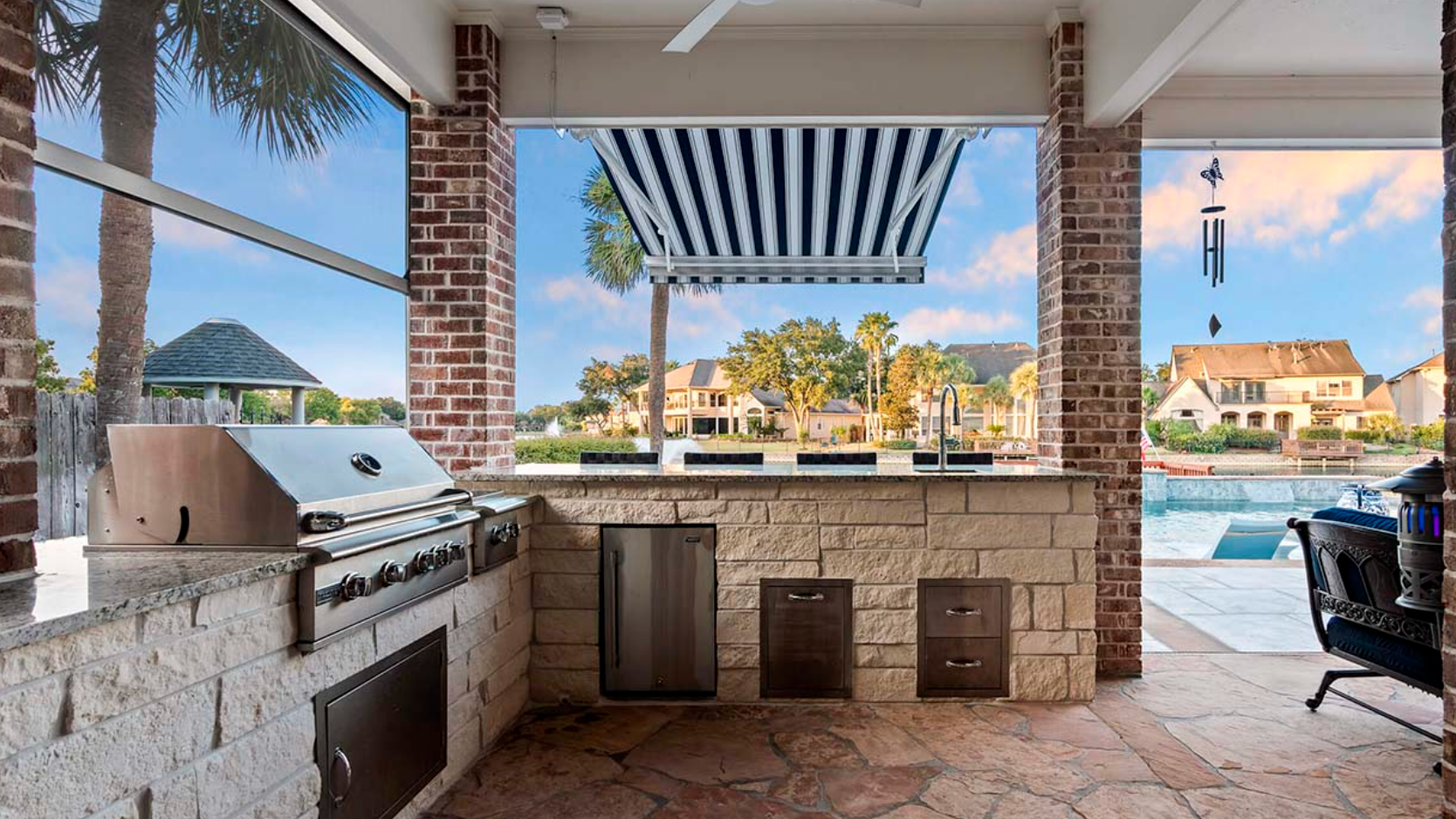 A large outdoor kitchen with a grill and a swimming pool in the background.