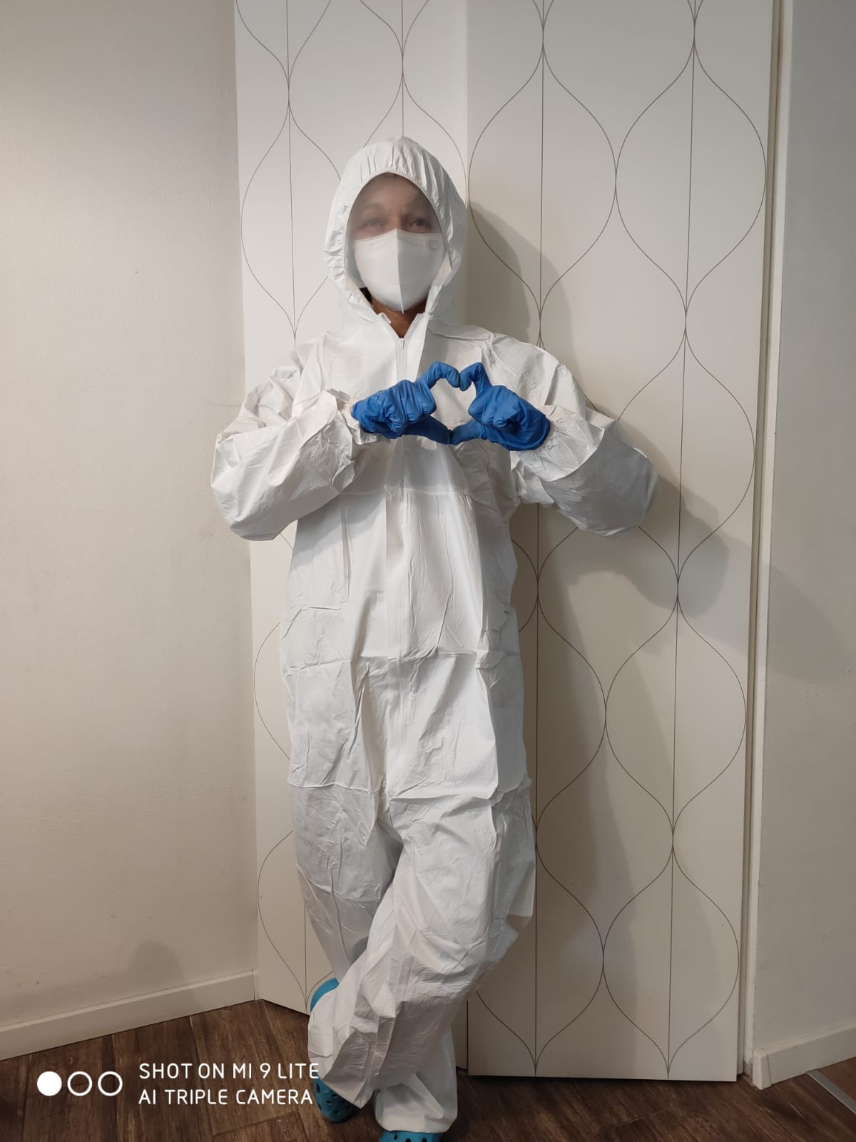 Una donna con tuta protettiva e maschera sta disegnando un cuore con le mani.