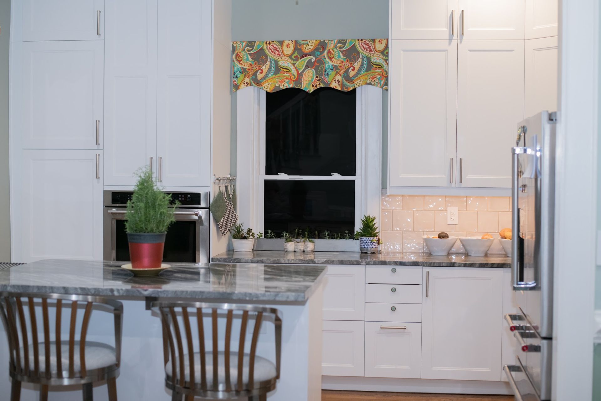 A kitchen with white cabinets , granite counter tops , stainless steel appliances and a window.