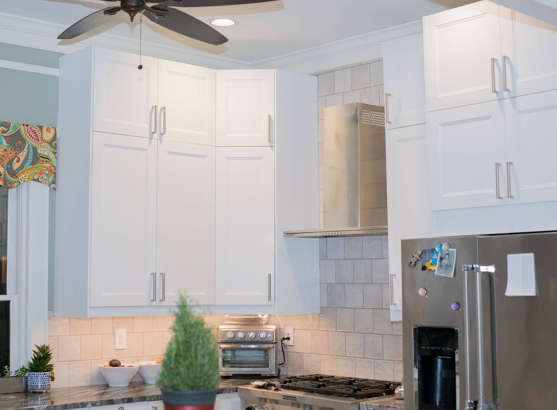 A kitchen with white cabinets , stainless steel appliances and a ceiling fan.