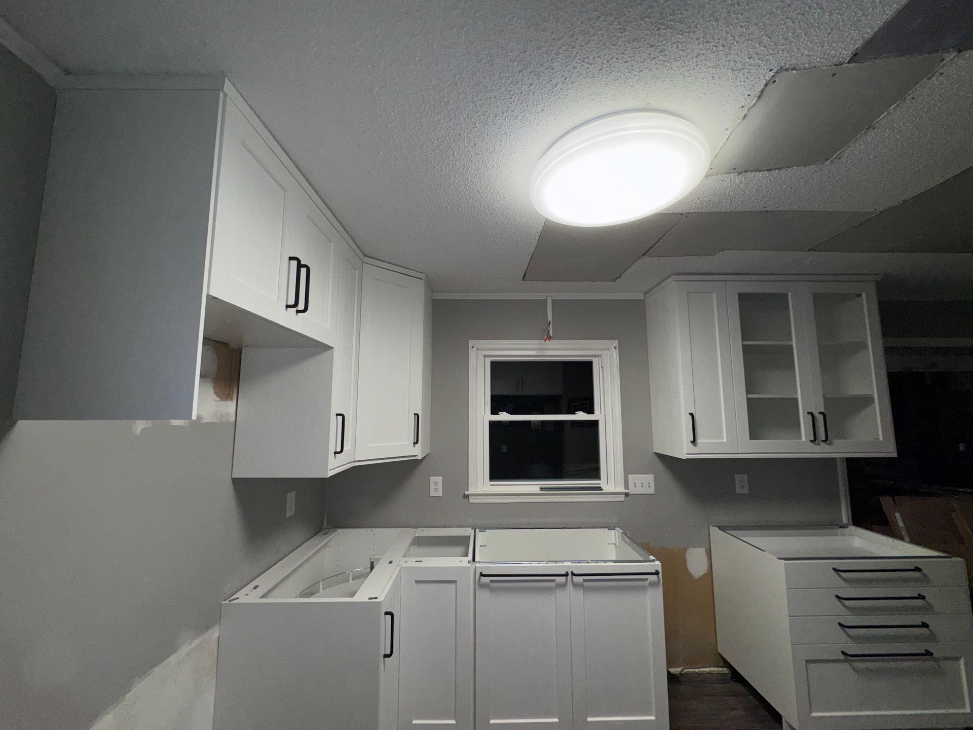 A kitchen under construction with white cabinets and a window.