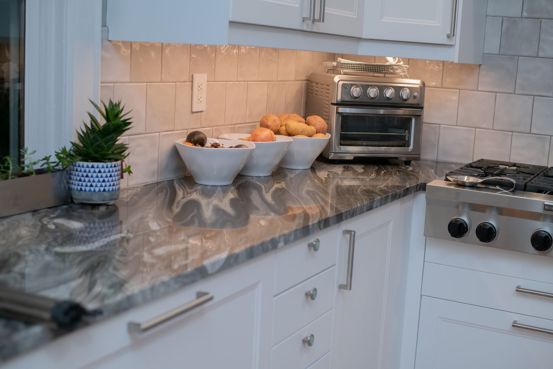 A kitchen with white cabinets , granite counter tops , a stove and a toaster oven.