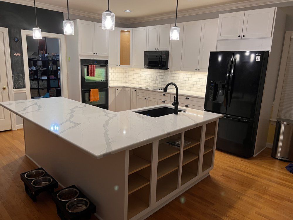 A kitchen with white cabinets , a black refrigerator , a sink , and a large island.
