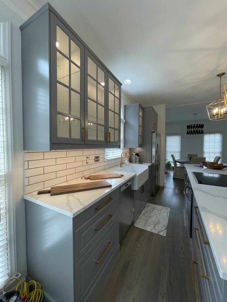 A kitchen with gray cabinets and white counter tops.
