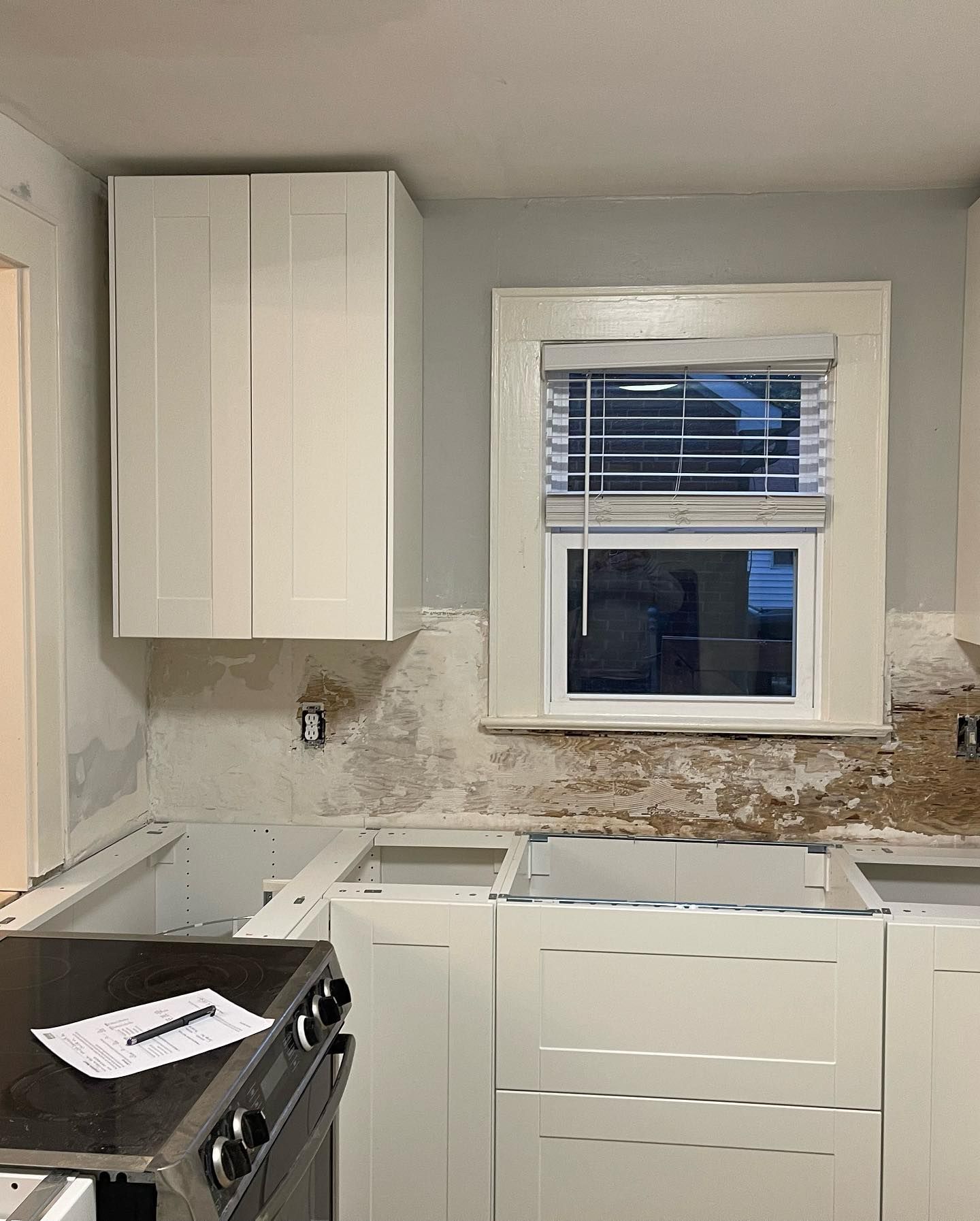 A kitchen with white cabinets , a stove , and a window.