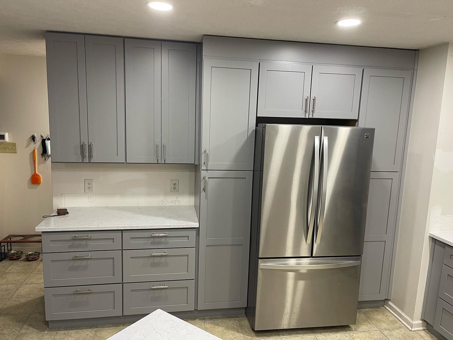 A kitchen with gray cabinets and a stainless steel refrigerator.