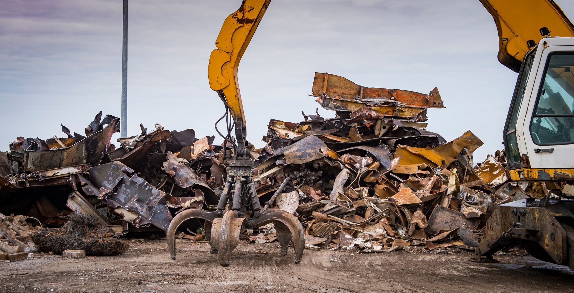 An industrial claw crane moving metal debris at a busy scrap metal recycling center for processing