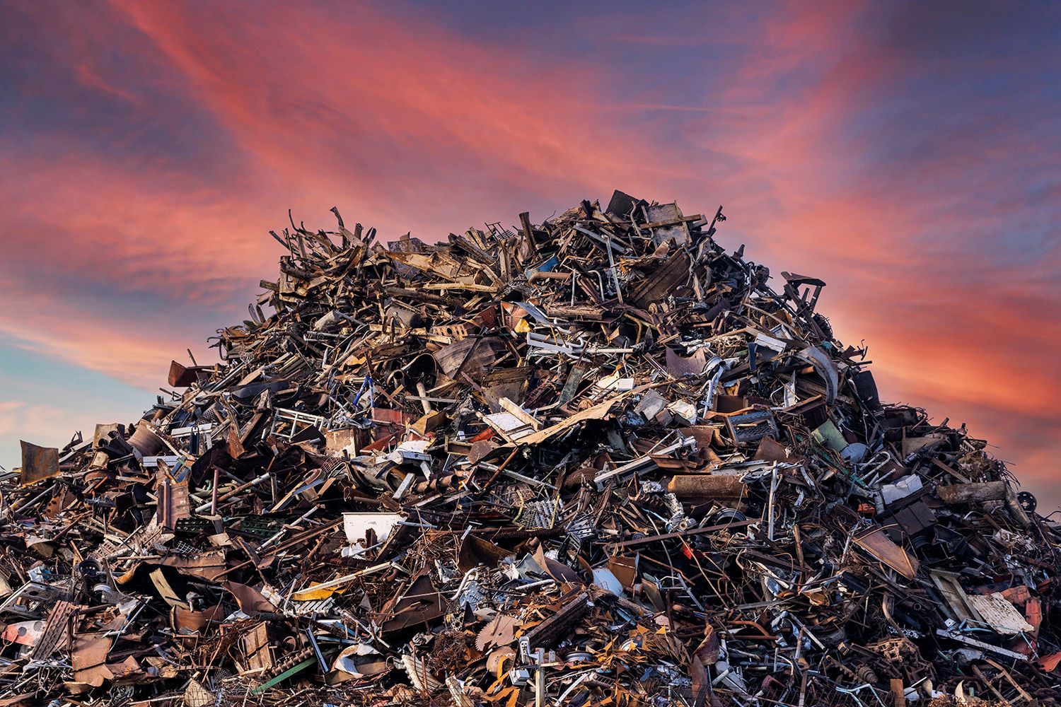 Large pile of scrap metal and debris under a colorful sunset sky. Large pile of scrap metal and debris under a colorful sunset sky.