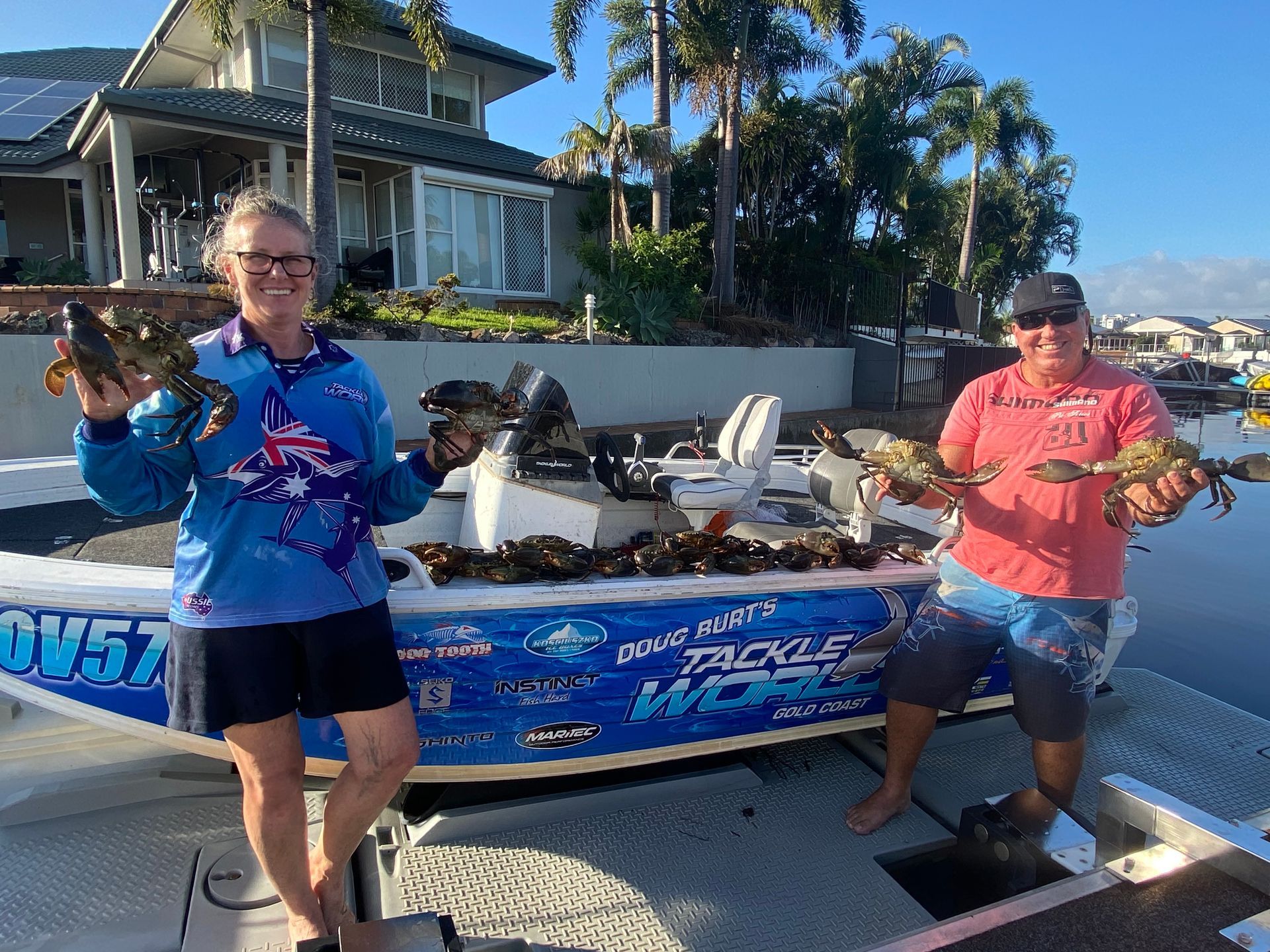 A man and a woman are standing next to a boat holding crabs.