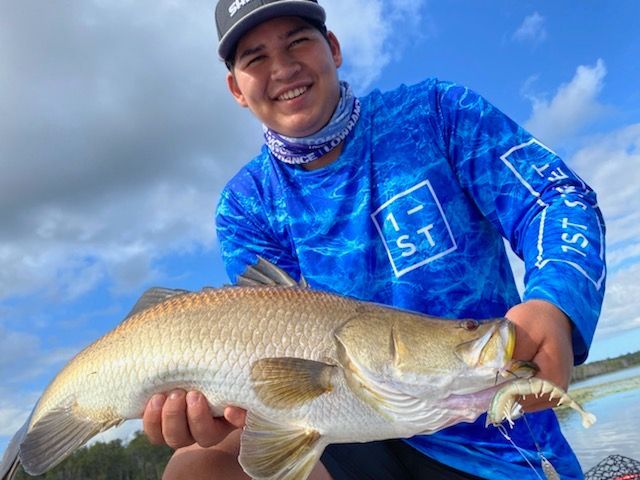 A man in a blue shirt is holding a large fish in his hands.