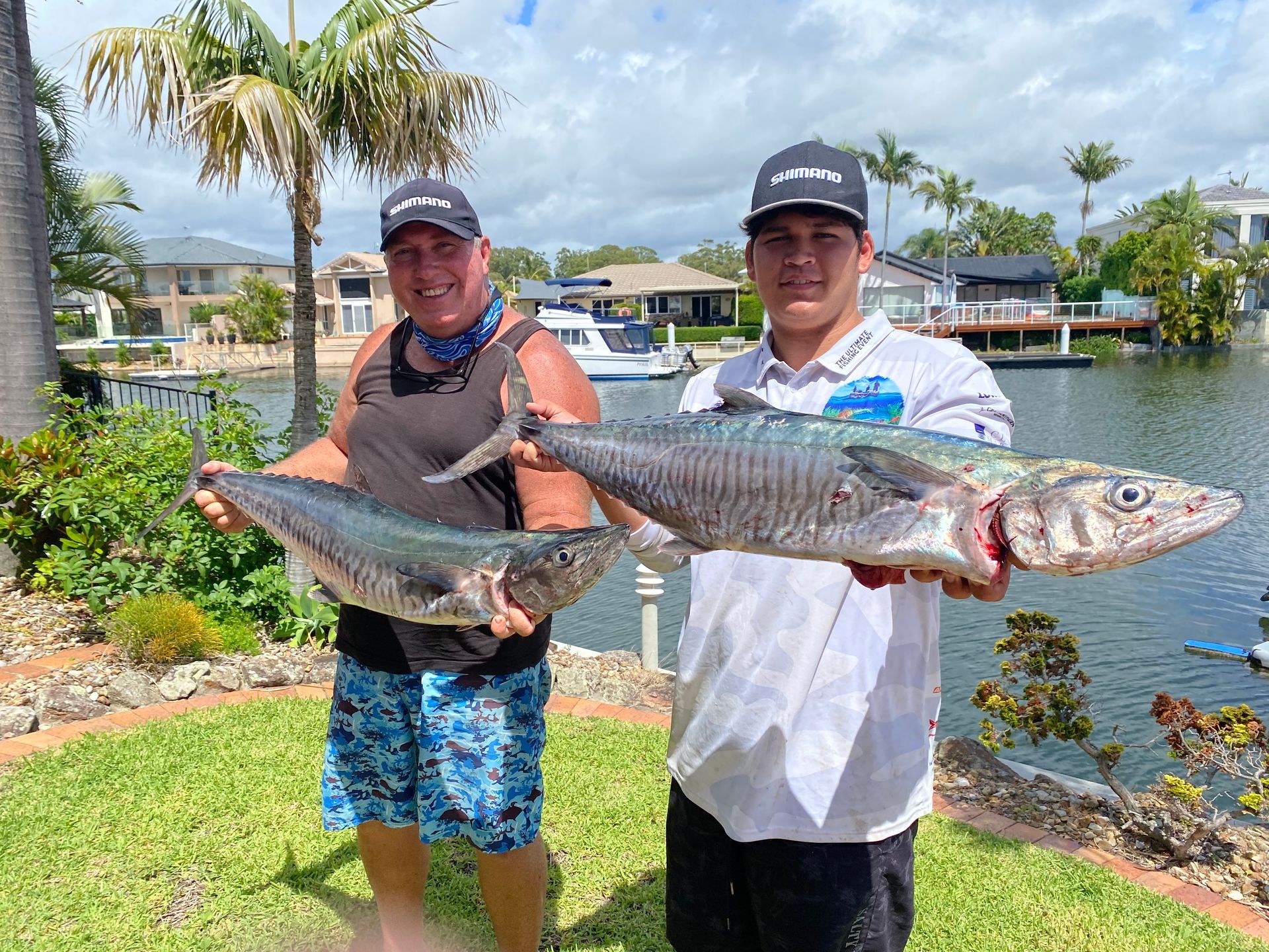 Two men are holding two large fish in front of a body of water.
