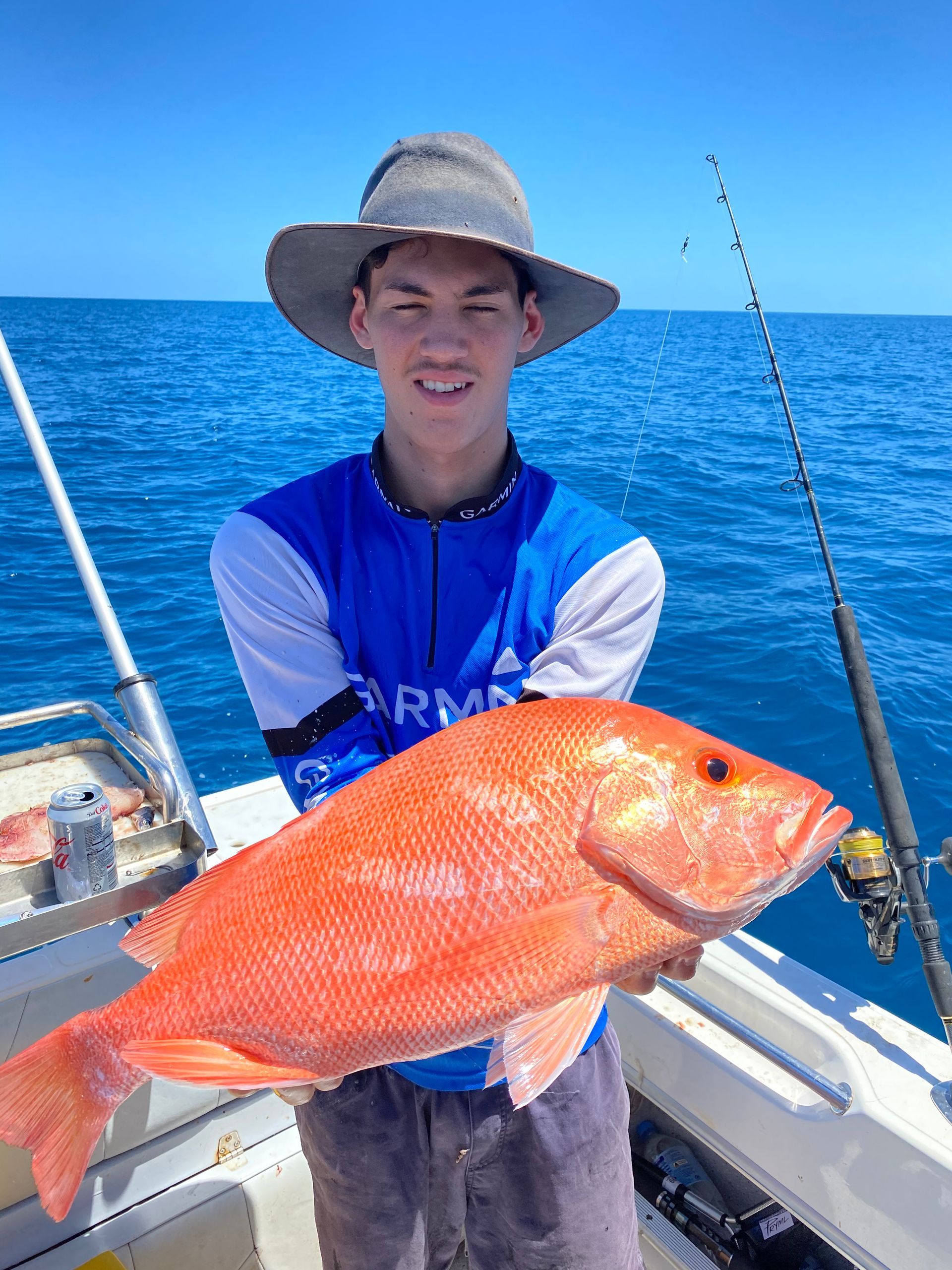 A young man is holding a large red fish on a boat.