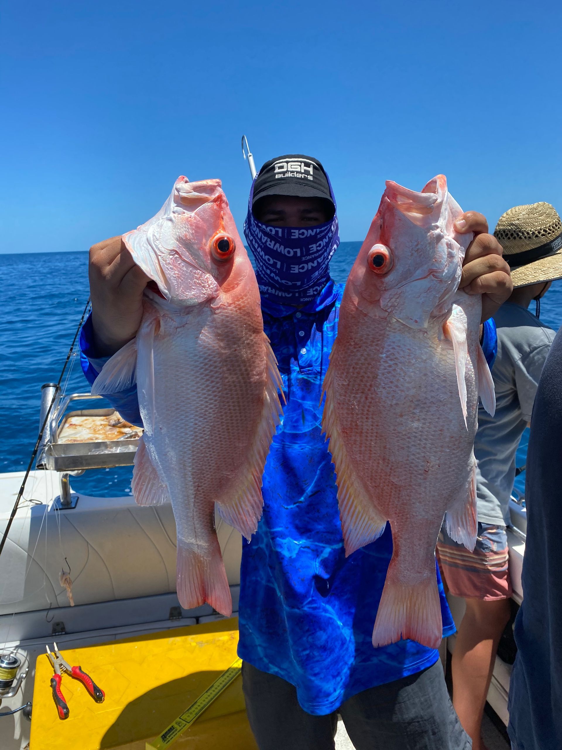 A man is holding two fish in his hands on a boat.