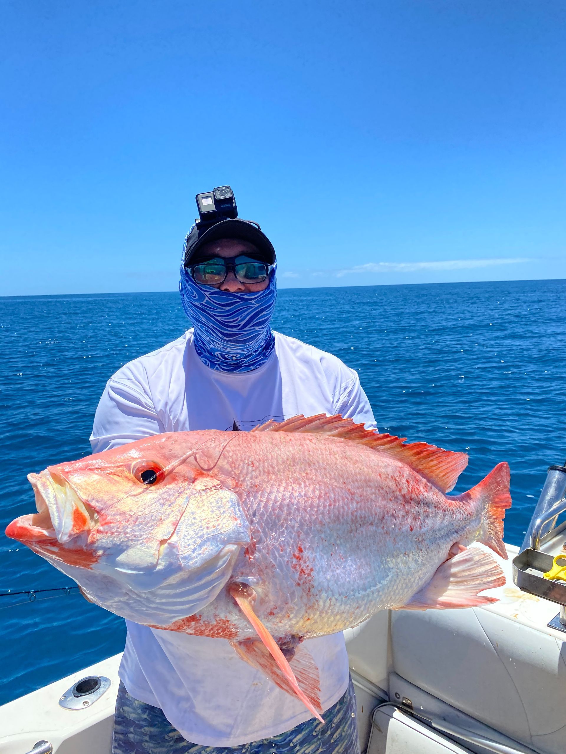 A man is holding a large red fish on a boat in the ocean.