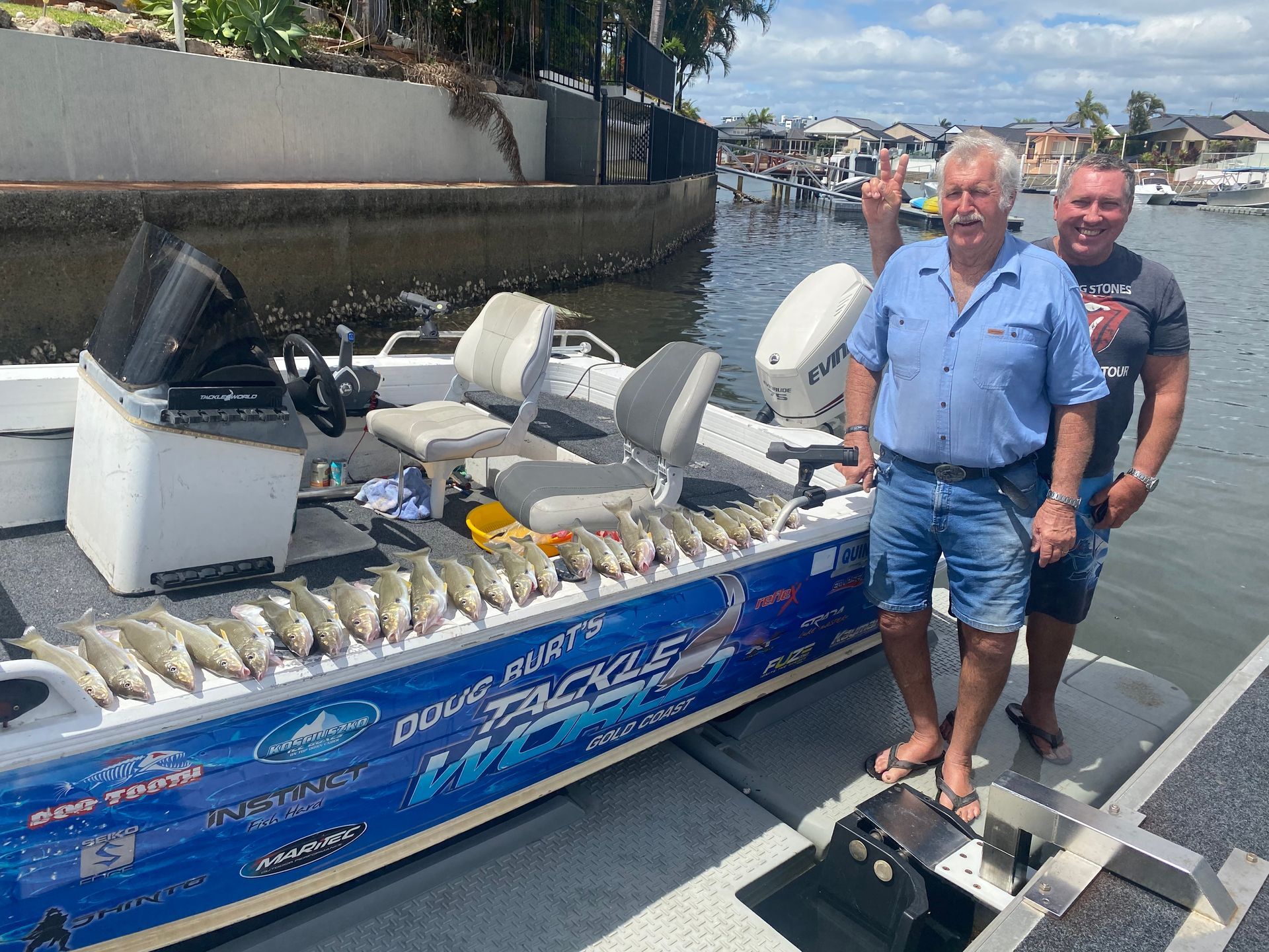 Two men are standing next to a boat filled with fish.