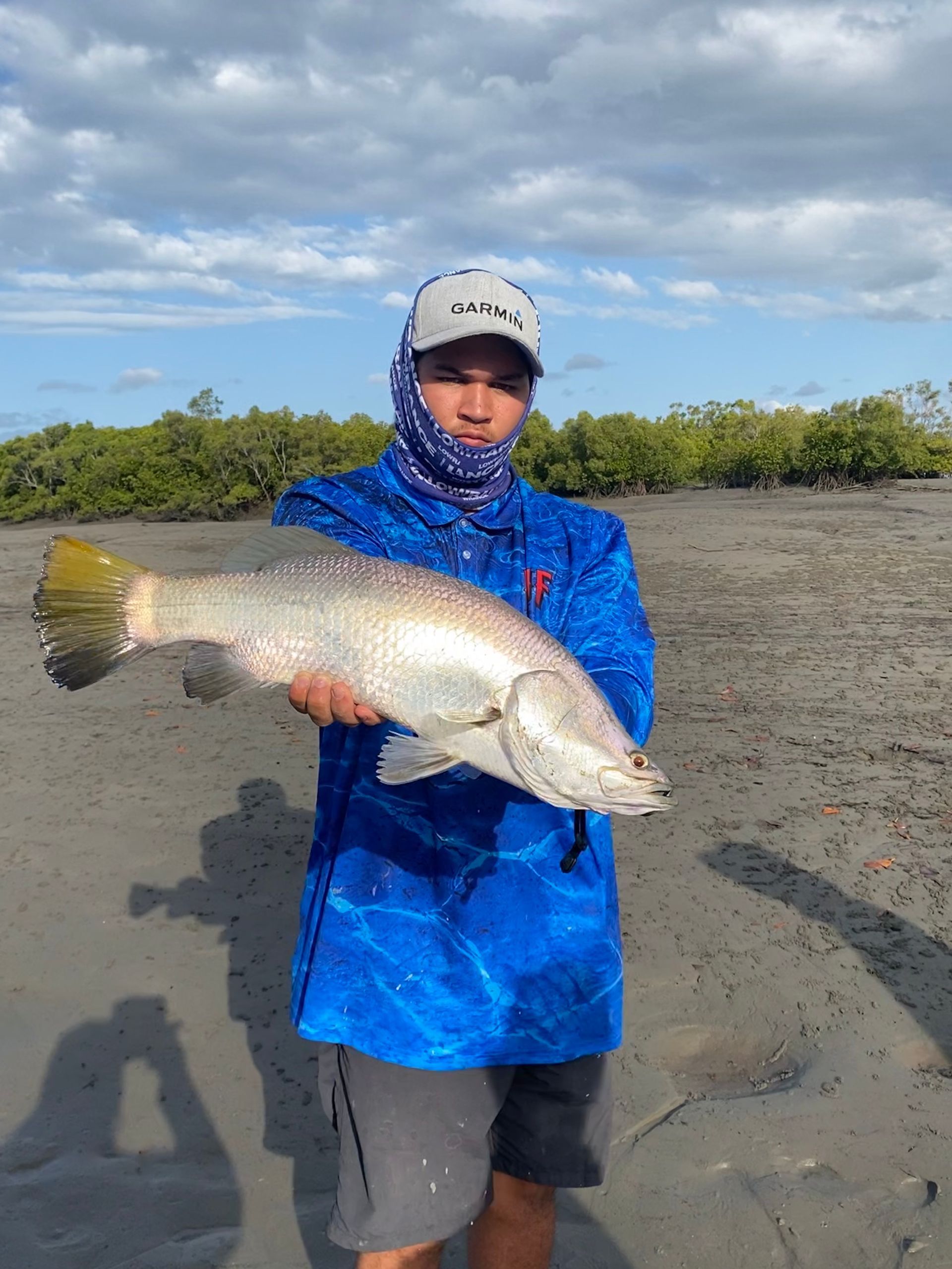 A man in a blue shirt is holding a large fish on the beach.
