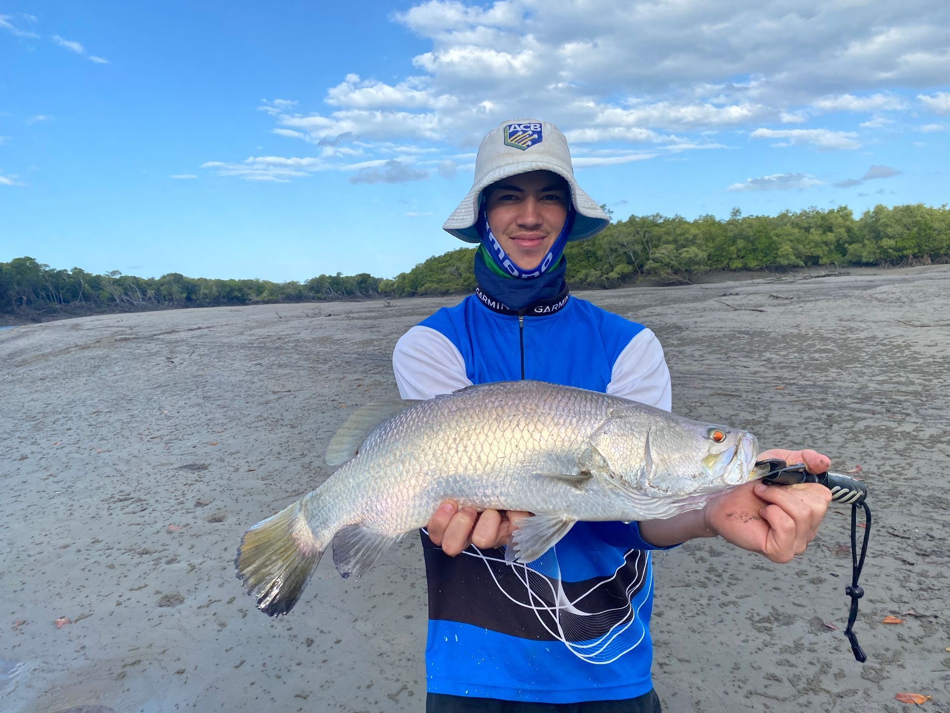 A young man is holding a large fish on the beach.