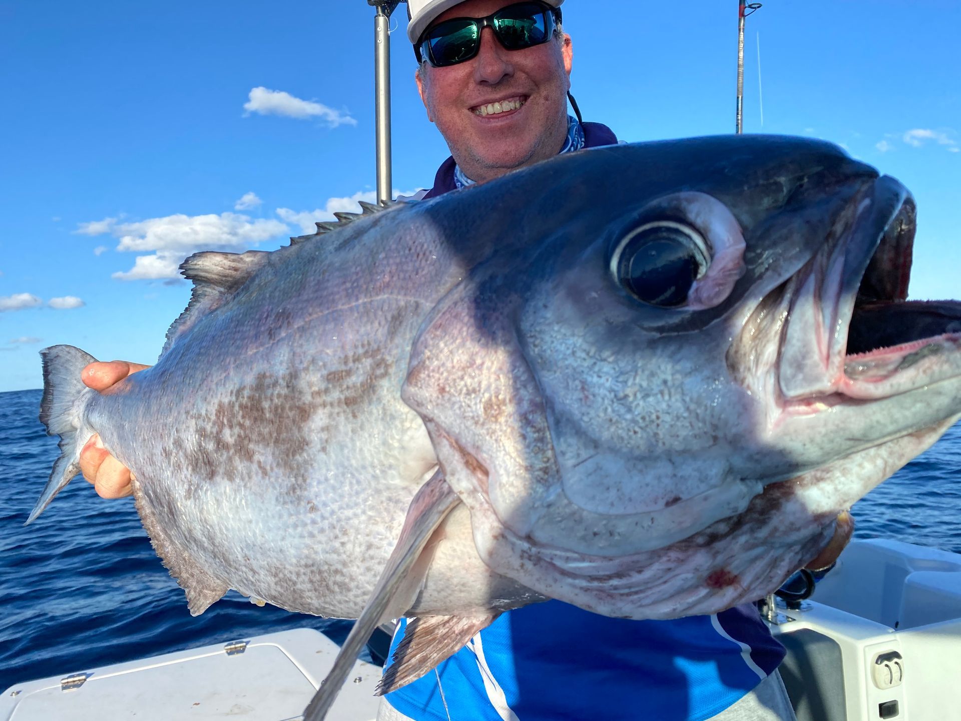 A man is holding a large fish on a boat in the ocean.