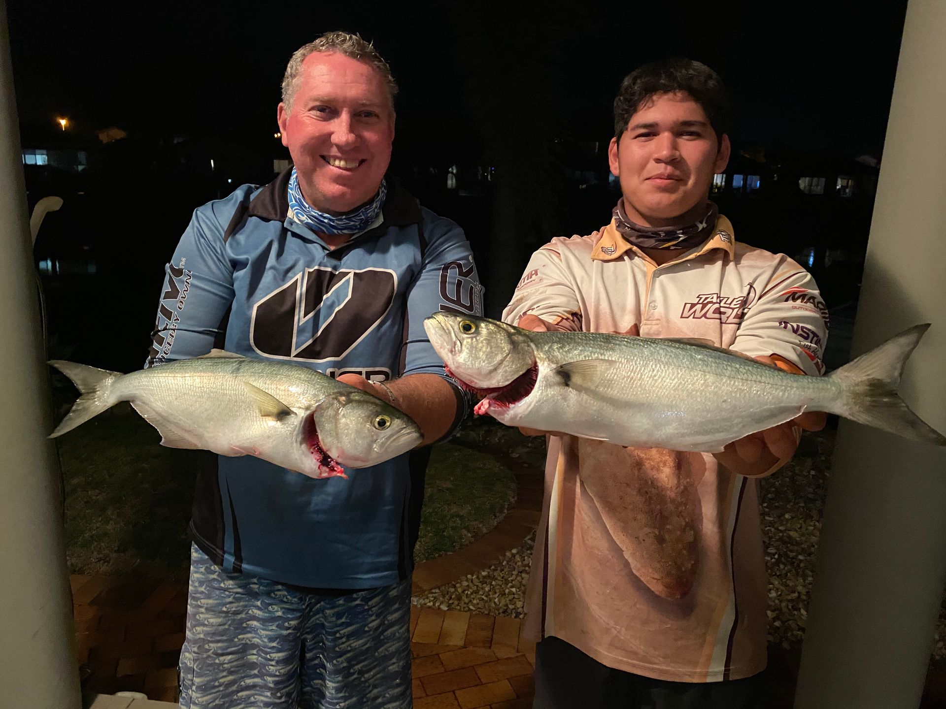 Two men are holding two fish in their hands.