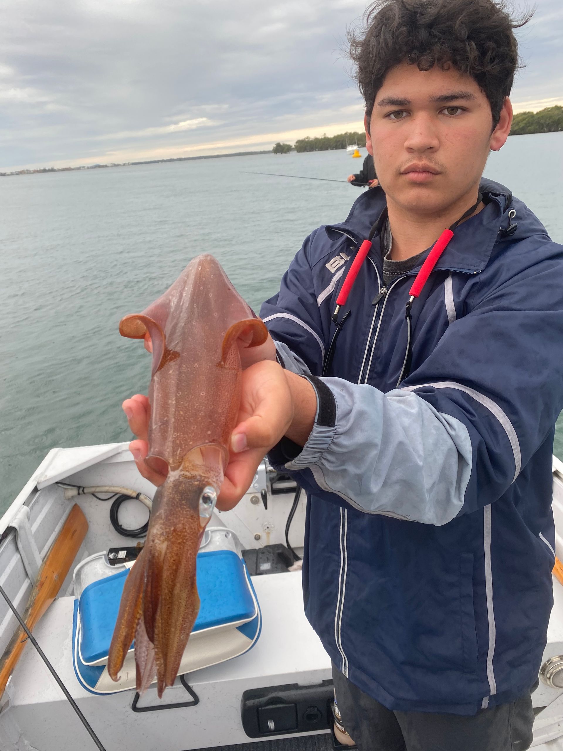 A young man is holding a squid in his hands on a boat.