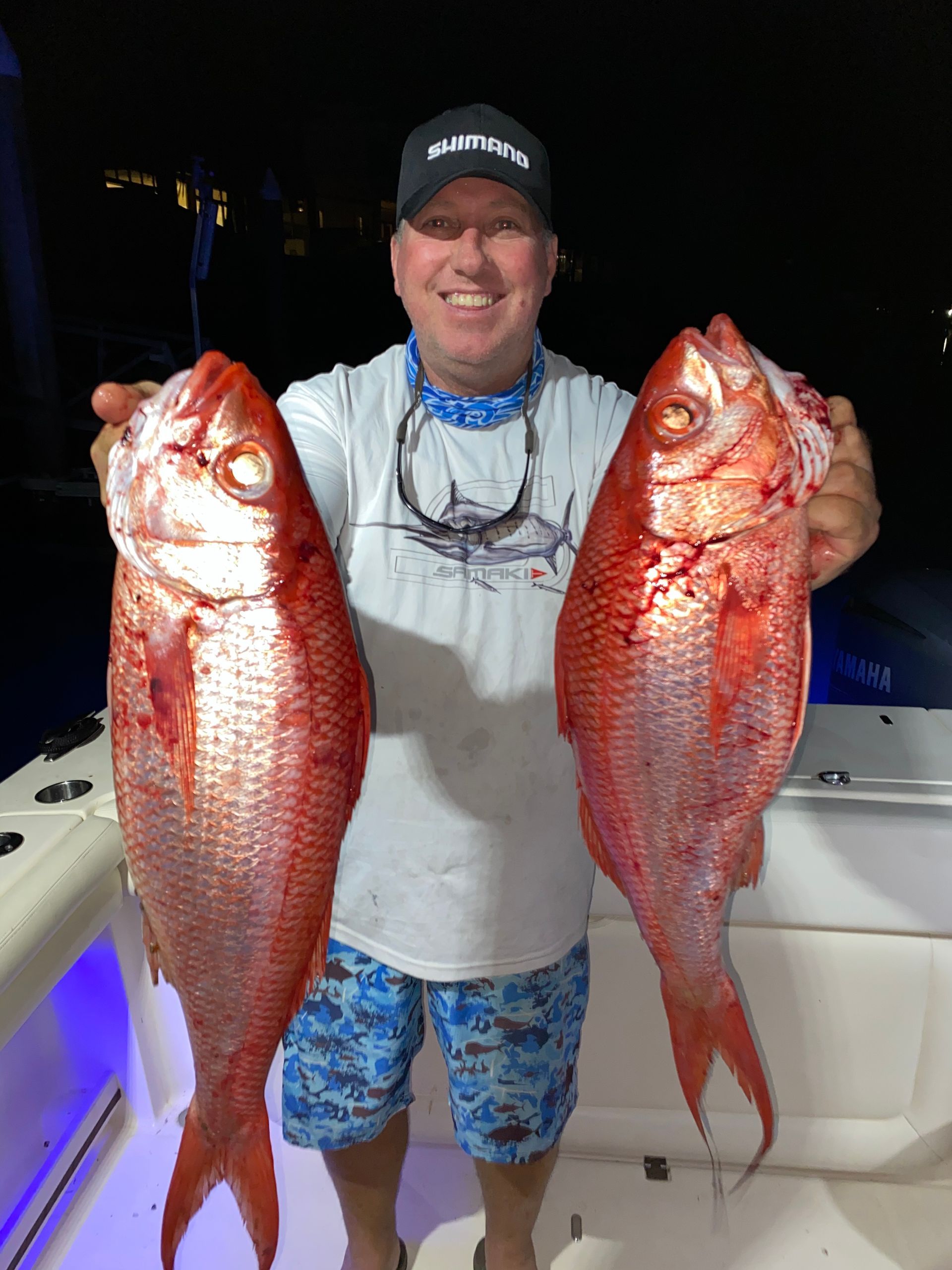 A man is holding two large red fish in his hands.