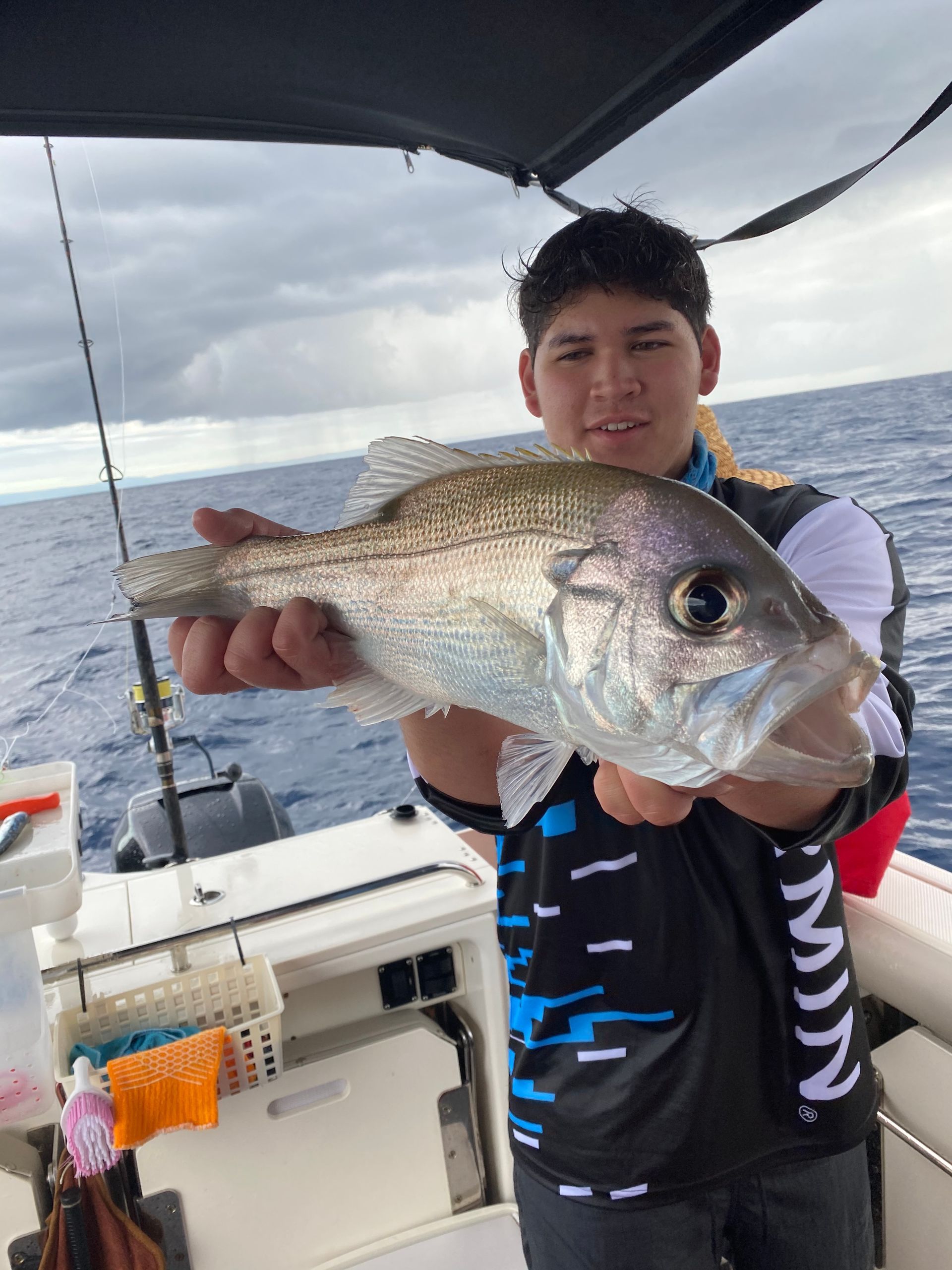 A young boy is holding a fish on a boat in the ocean.