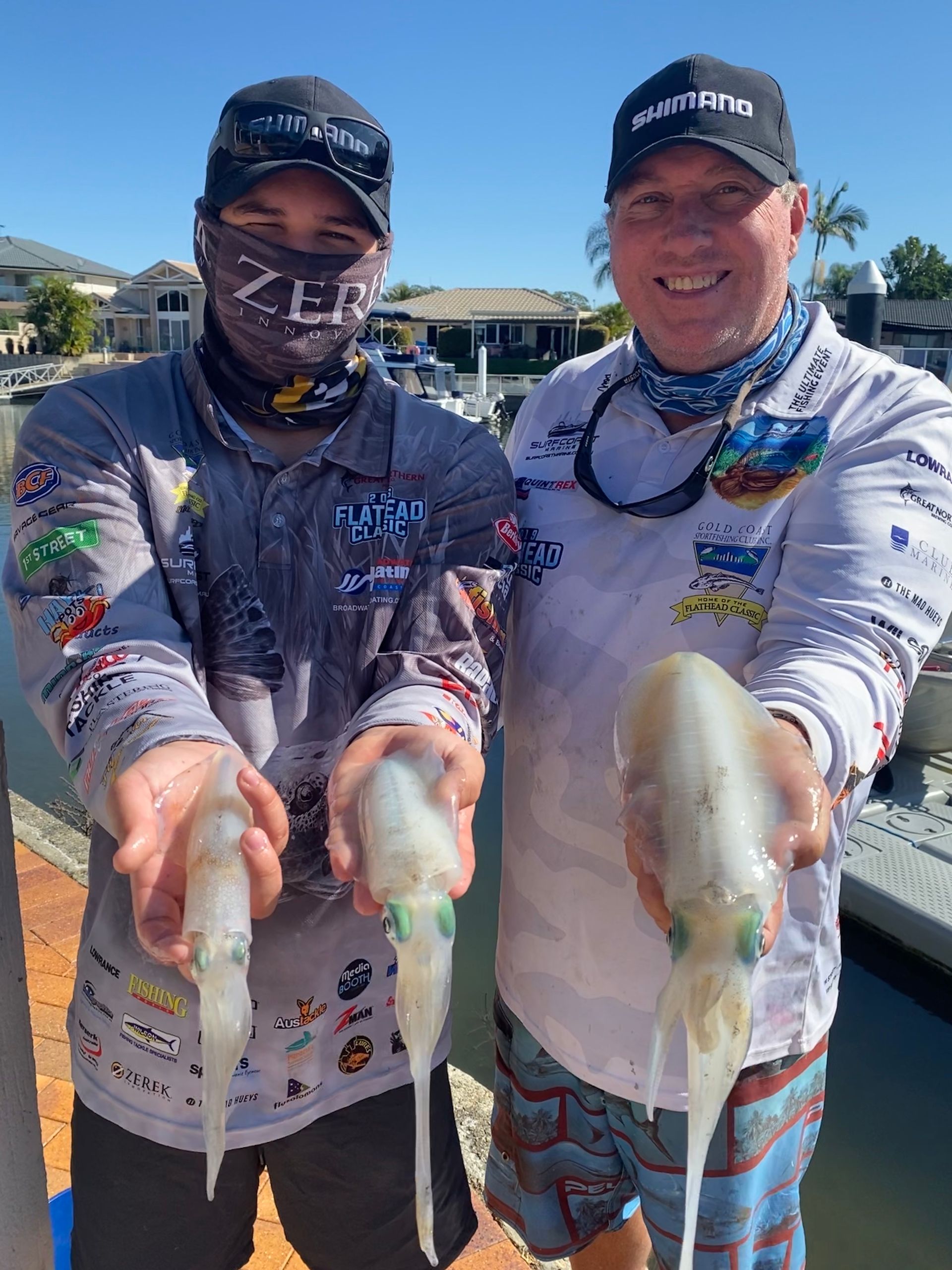 Two men are standing next to each other holding squid in their hands.