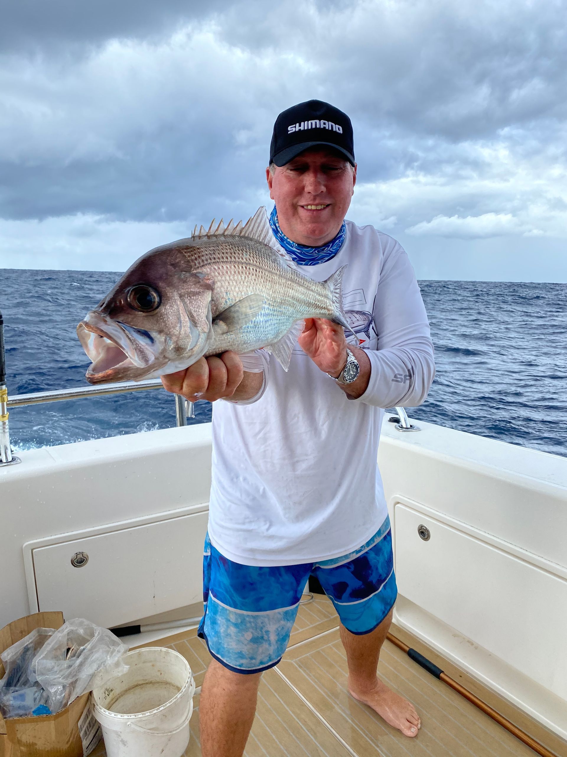 A man is holding a fish on a boat in the ocean.