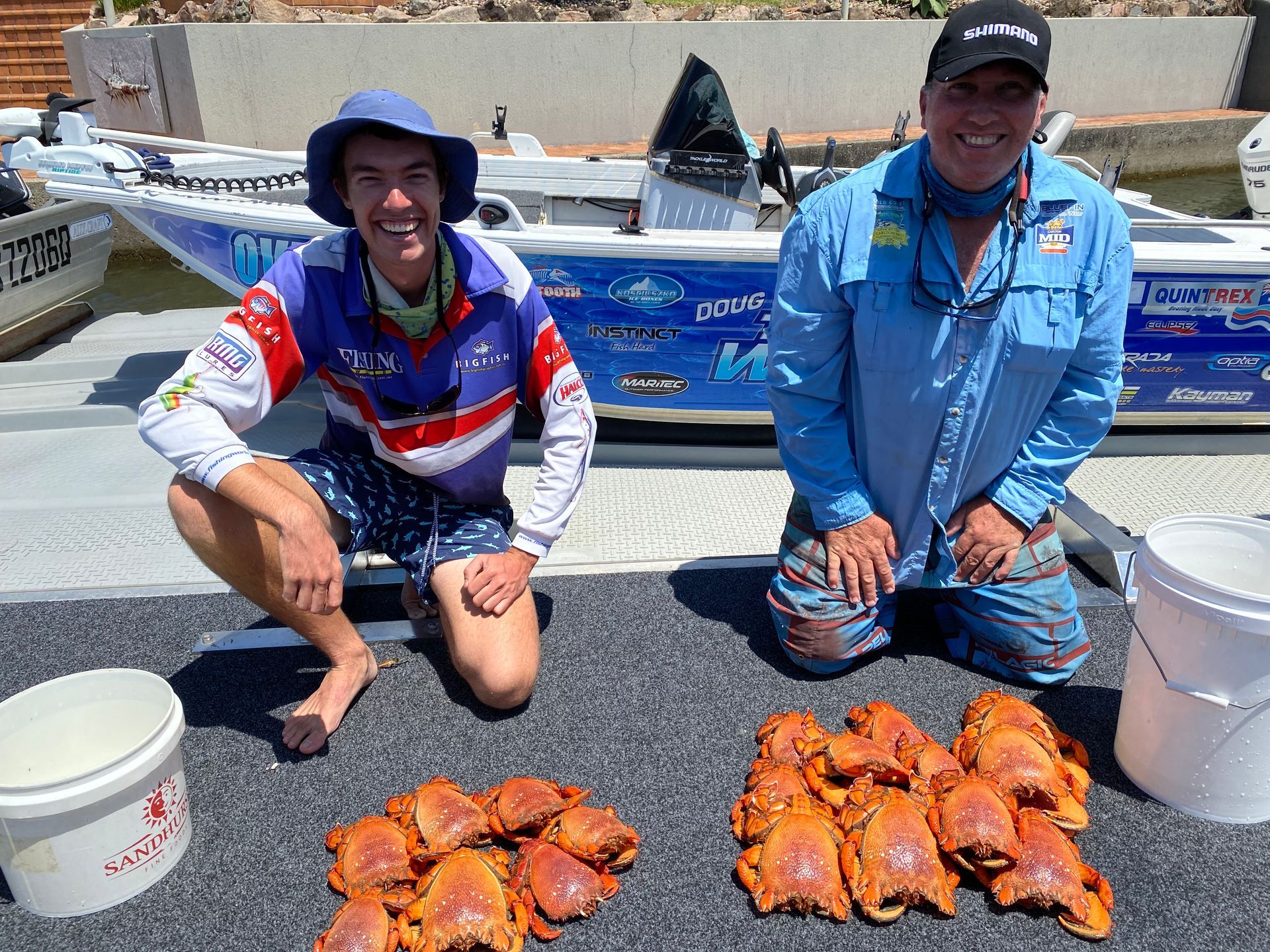 Two men are kneeling next to a pile of crabs in front of a boat.