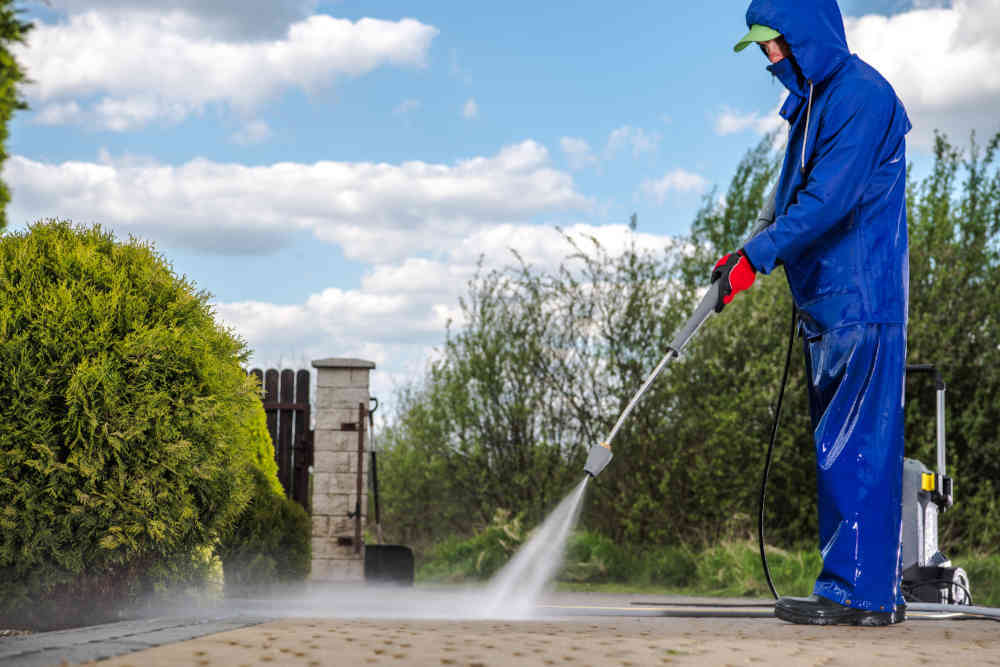A professional crew member power washing a paved driveway