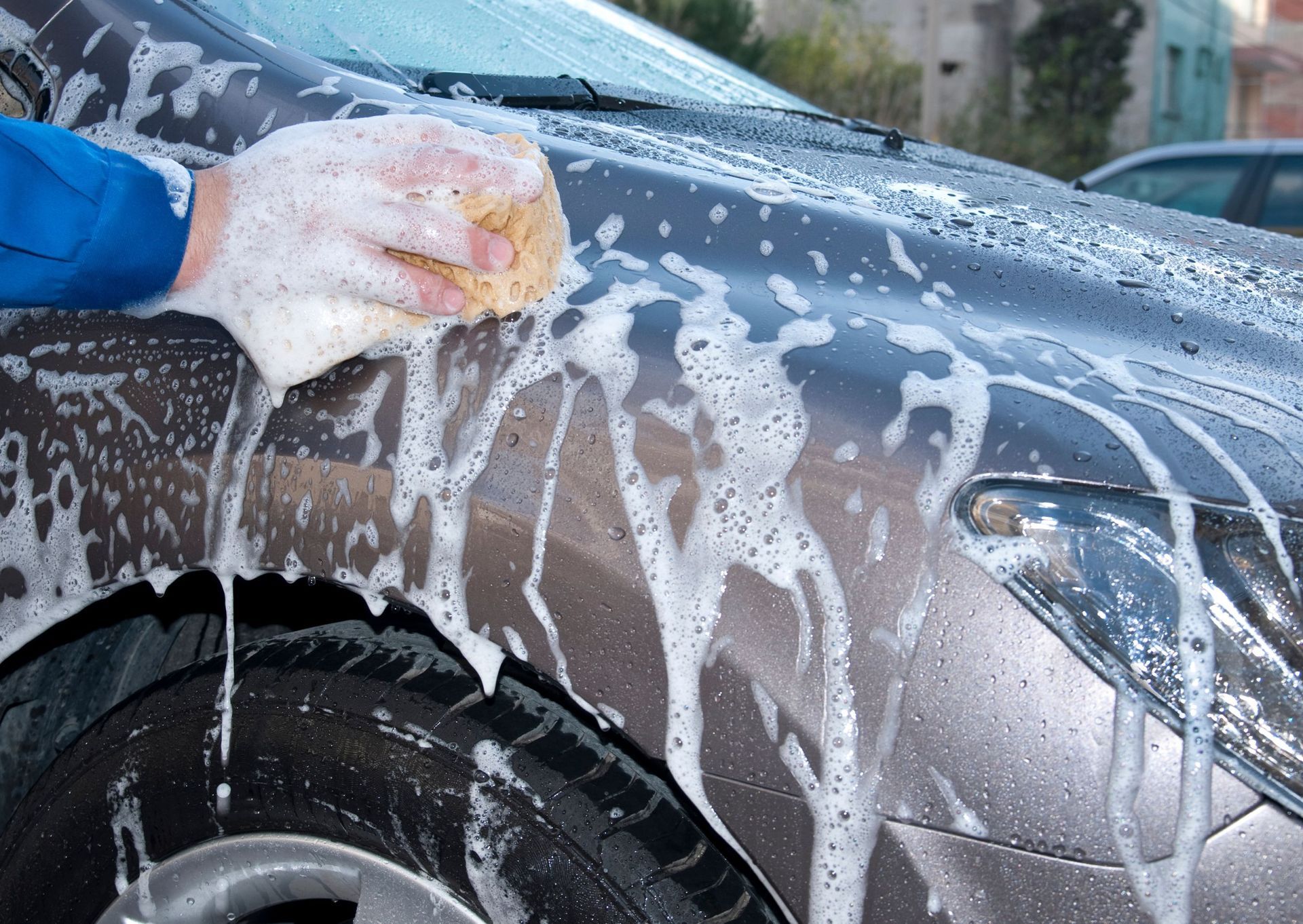 Person washing a brown car with a soapy sponge; outside.