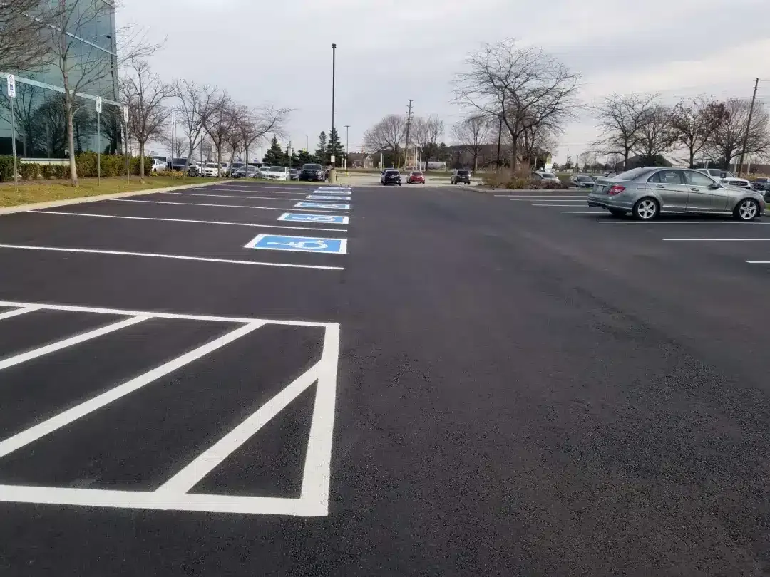 A freshly paved parking lot with marked accessible parking spaces and white painted lines under an overcast sky.