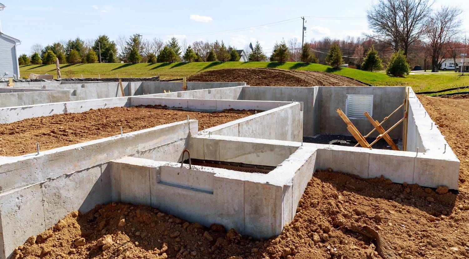 A concrete foundation for a new house under construction on a sunny, grassy lot.