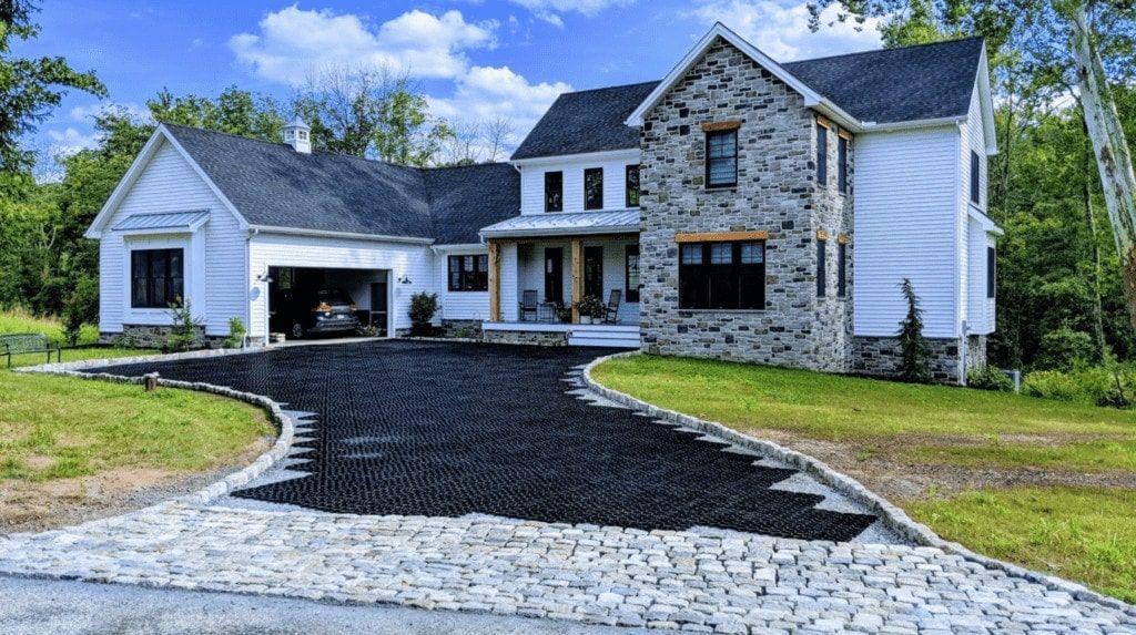 A two-story farmhouse with white siding and stone accents, featuring a dark gravel driveway and a stone-paved entrance.