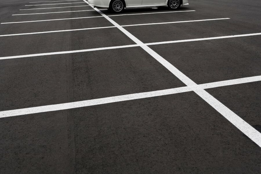 A white car parked in an empty parking lot with clearly marked white lines on the asphalt.