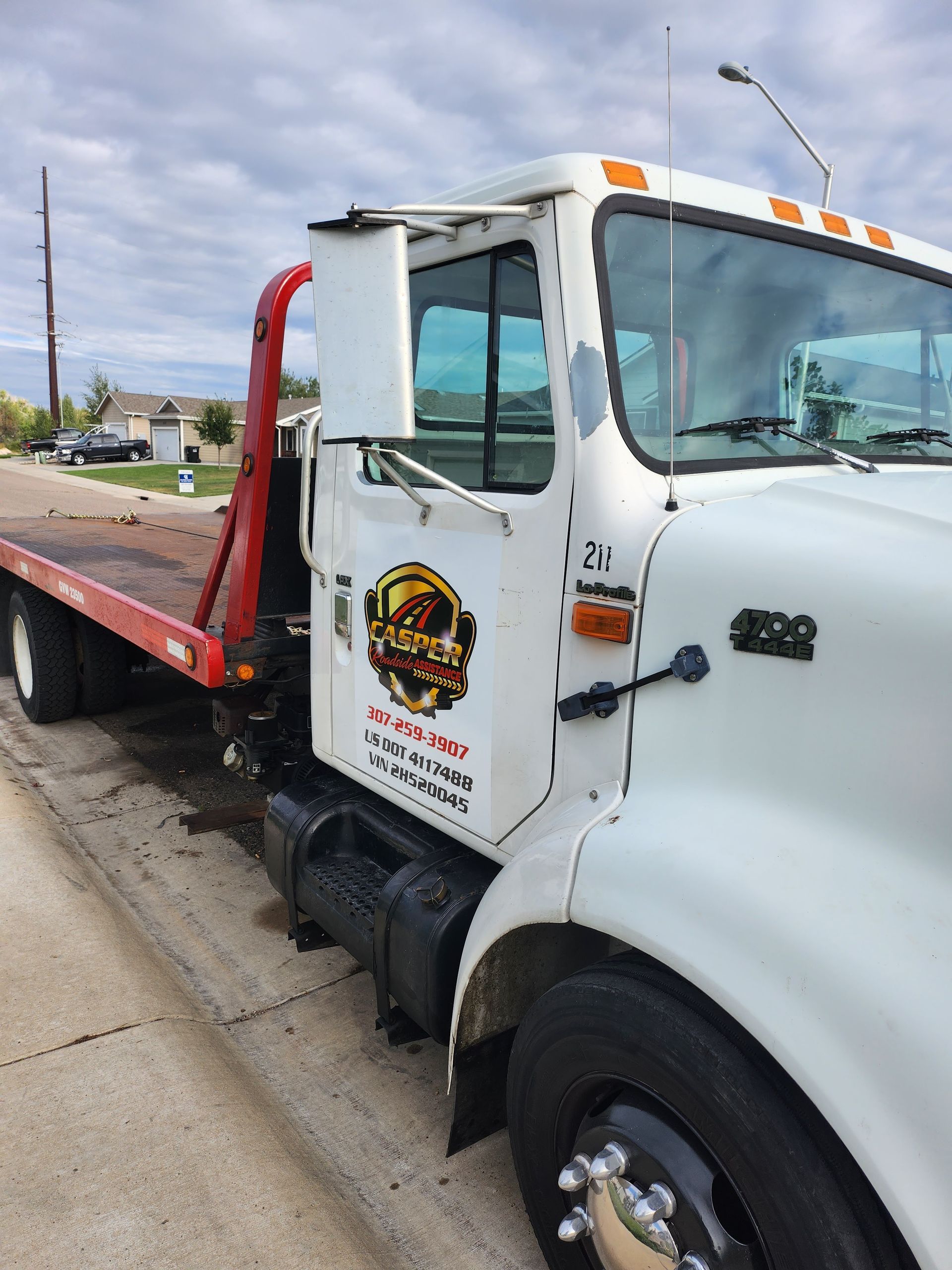 A white tow truck with a red flatbed is parked on the side of the road.