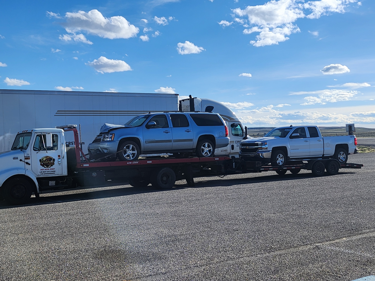 A tow truck is carrying a silver suv and a white truck.