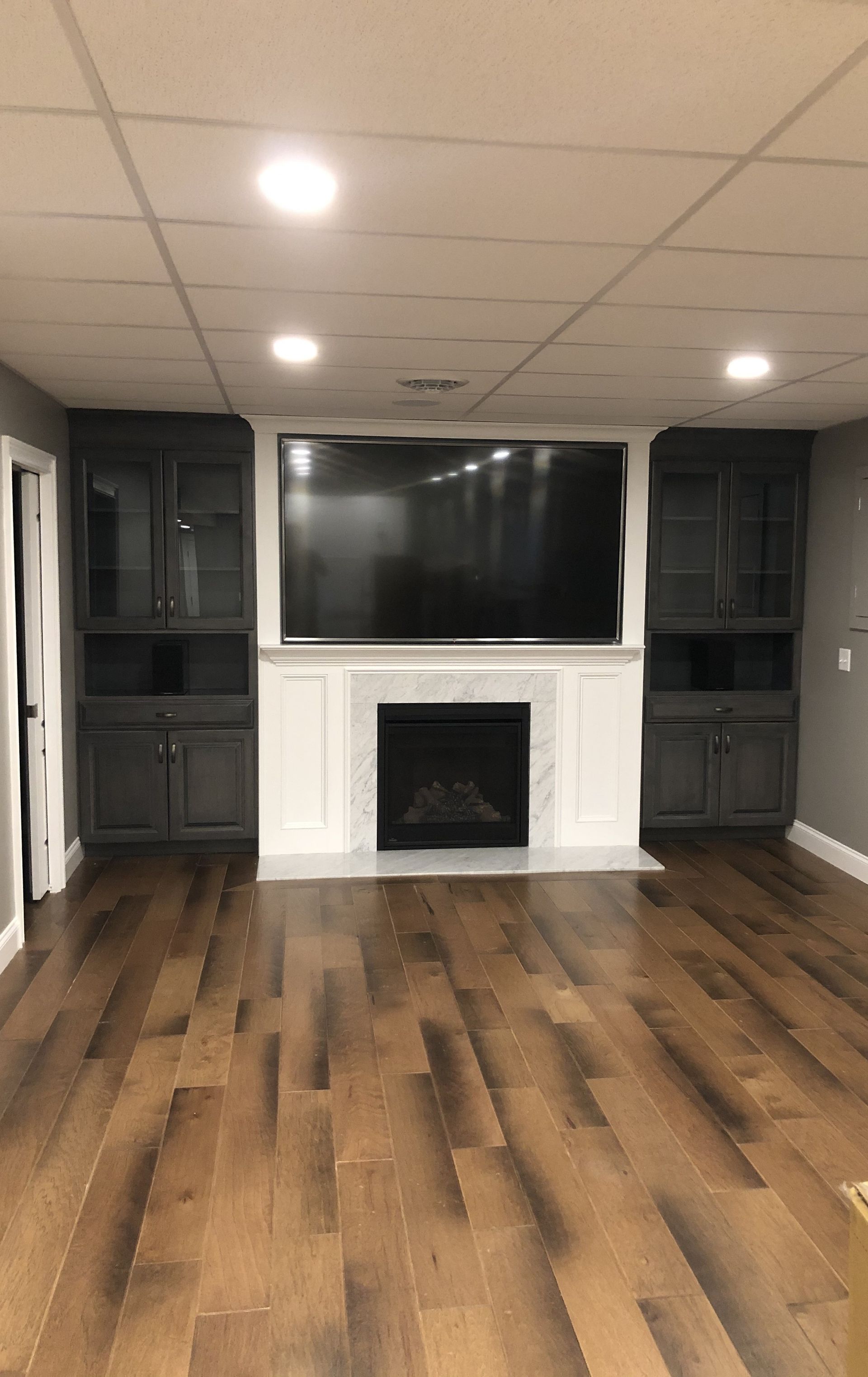 Empty living room with wood floors, white fireplace, wall-mounted TV, and built-in cabinets