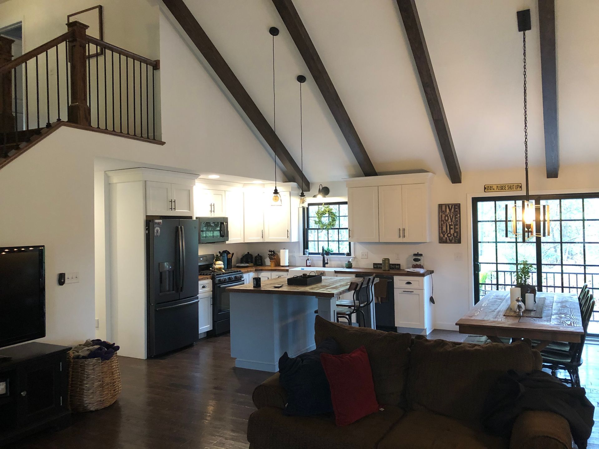 Open-concept living room and kitchen with vaulted ceiling, dark beams, and large windows